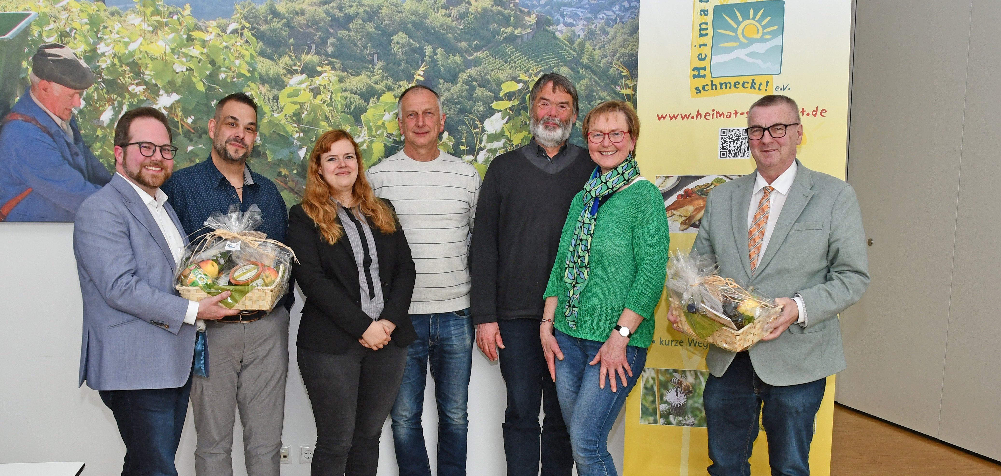 Die Geschäftsführerin Sophie Ewald (3.v.l.), der Vorsitzende Michael Klein (2.v.l.) sowie die Gründungsmitglieder Marie-Theres Neumann (2.v.r.) und Uwe Weber (Mitte) vom Verein Heimat schmeckt! e.V. übergaben Landrat Dr. Alexander Saftig (rechts) und dem Ersten Kreisbeigeordneten Pascal Badziong (links) zwei Präsentkörbe anlässlich des 20-jährigen Jubiläums von Heimat schmeckt! e.V.. Dr. Rüdiger Kape (3.v.r.) von der Integrierten Umweltberatung des Kreises freut sich mit allen Beteiligten, dass das Projekt erfolgreich auf eigenen Füßen steht. 