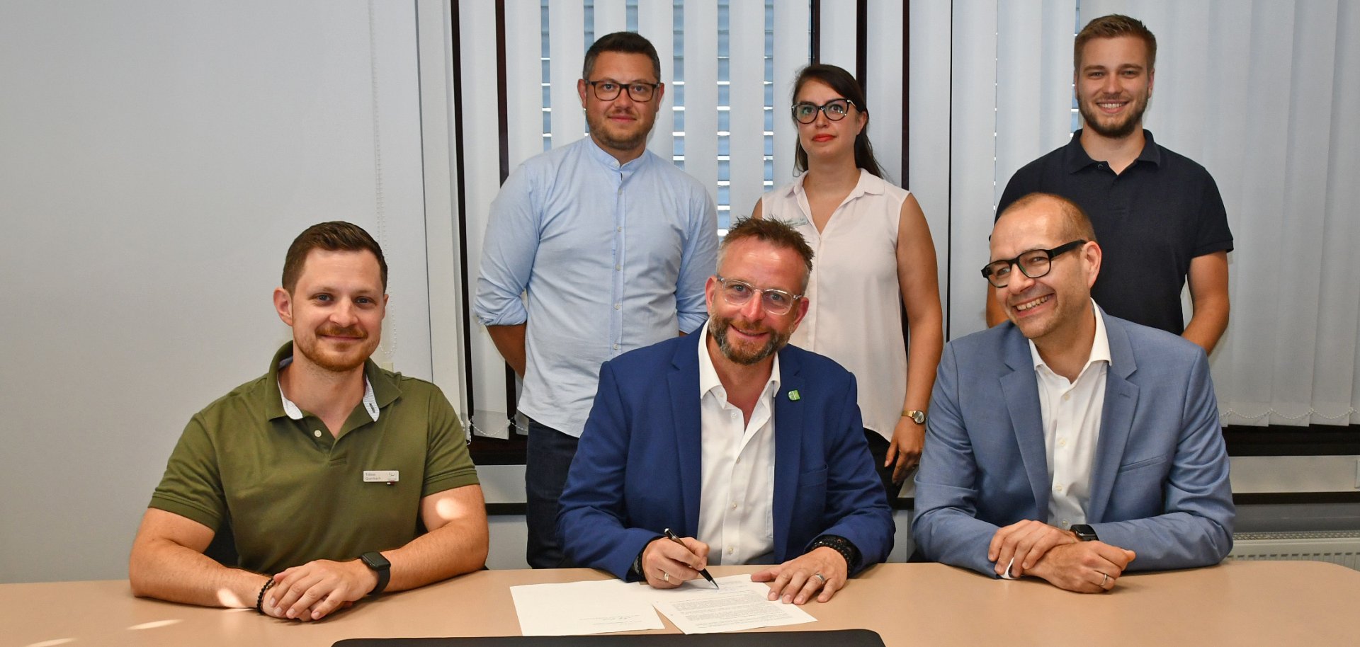 Landrat Marko Boos (vorne Mitte) und Prof. Dr. Wolfgang Kiess (vorne rechts) von der Hochschule Koblenz unterzeichneten den Vertrag zum Projekt RIOT im Beisein von Tobias Querbach (vorne links), CDO des Landkreises Mayen-Koblenz, der Projektmanagerin Tahmineh Bahadorizadeh (hinten Mitte) und weiteren Projektbeteiligten. 